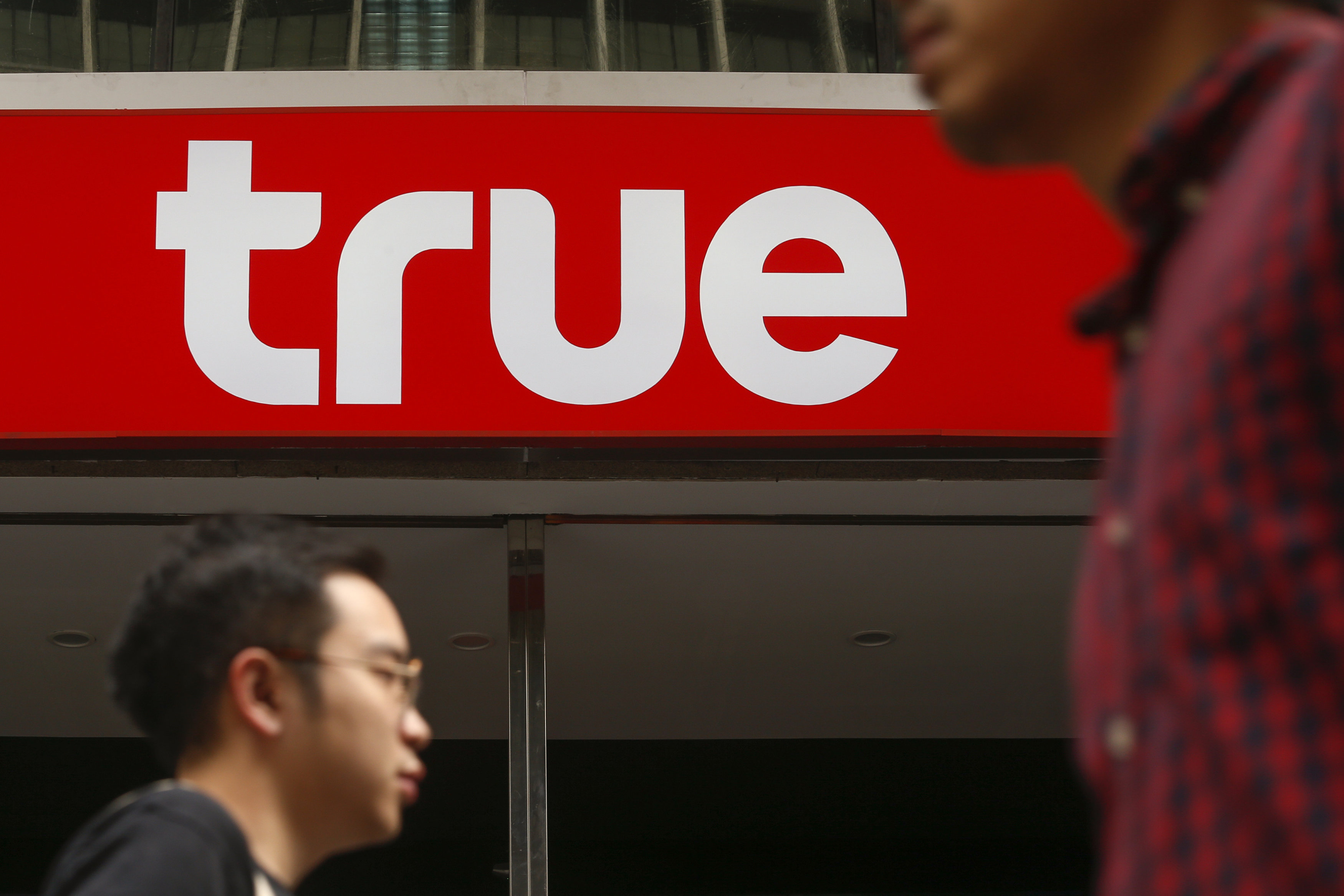 People walk past the logo of True Corp in Bangkok, Thailand, February 29, 2016. REUTERS/Athit Perawongmetha