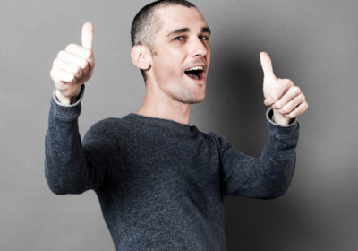 optimism concept - excited 30s man with short hair and thumbs up for congratulation or success, studio grey background, texture effects