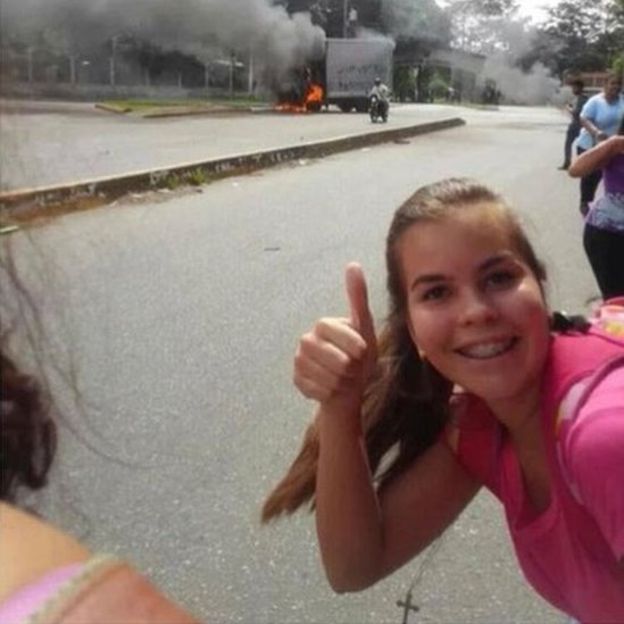 女孩在焚燒中的貨車前豎起拇指，表示一切情況良好。圖片來源：BBC