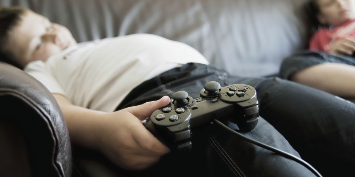 Boys Sleeping On Sofa While Holding Games Consoles